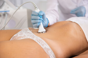 Female patient undergoing ultrasonic cavitation procedure on belly at modern aesthetic medicine...