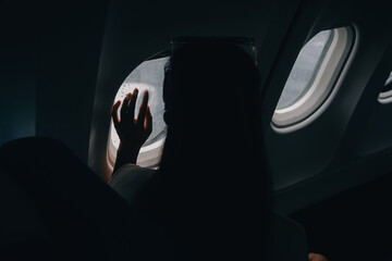 Silhouette of woman looks out the window of an flying airplane. Passenger on the plane resting...