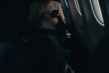 Fototapeta na wymiar Attractive Asian female passenger of airplane sitting in comfortable seat while working laptop and tablet with mock up area using wireless connection. Travel in style, work with grace.
