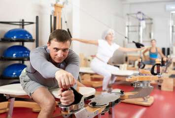 Adult man in sportswear stretches her arms and shoulders using pilates machine..