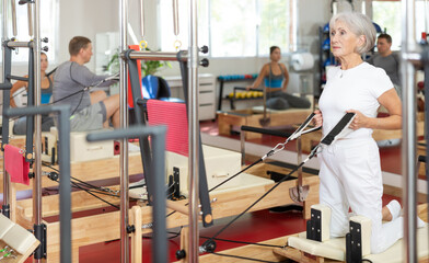 Elderly athletic woman working out with straps in pilates studio..