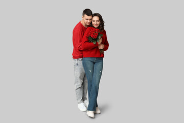 Loving young couple with bouquet of beautiful roses on grey background. Celebration of Saint...