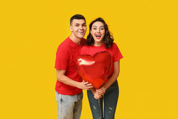 Loving young couple with heart-shaped balloon on yellow background. Celebration of Saint...