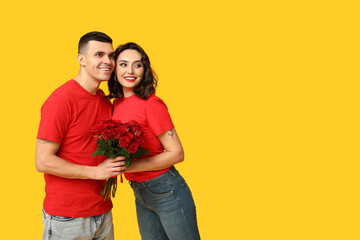 Loving young couple with bouquet of beautiful roses on yellow background. Celebration of Saint...