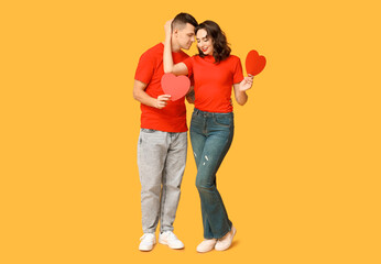 Loving young couple with paper hearts on yellow background. Celebration of Saint Valentine's Day