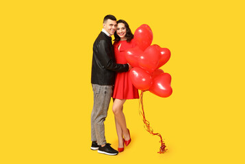 Loving young couple with heart-shaped balloons on yellow background. Celebration of Saint...