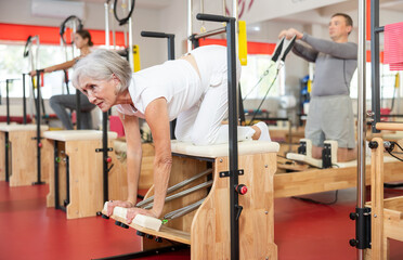Elderly woman in sportswear working out using pilates machine in pilates studio..