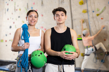 Motivated sporty young people, man and woman standing with special equipment before climbing up bouldering wall in amusement center