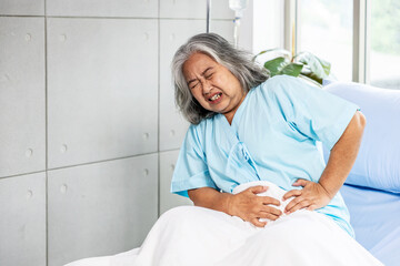 Asian elderly woman has a stomachache, severe abdominal pain, She sat on the bed, The concept of...
