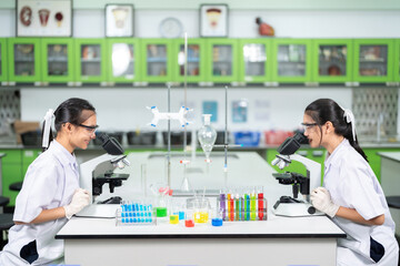 Fototapeta premium Vaccine and virus research in the lab of two Asian female scientists using a microscope to look at germs There are equipment such as glass tubes, beakers, and chemicals in medical biology.