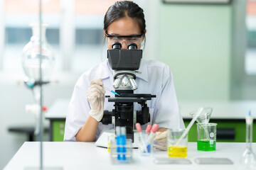 Asian female scientist is a student doing lab experiments with a microscope. Holding a glass tube...