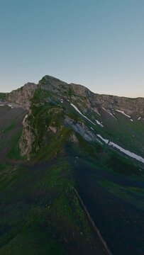 Vertical video. Aerial view mountain ridge peak ski resort cable car extreme close rock natural wall stone texture snow sunset. FPV sport drone amazing shot cliff alpine valley morning sunrise grass