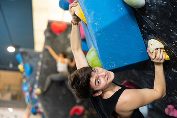 Cheerful concentrated young male busy with his hobby bouldering, climbing on artificial wall in gym, extreme sport, rock-climbing concept
