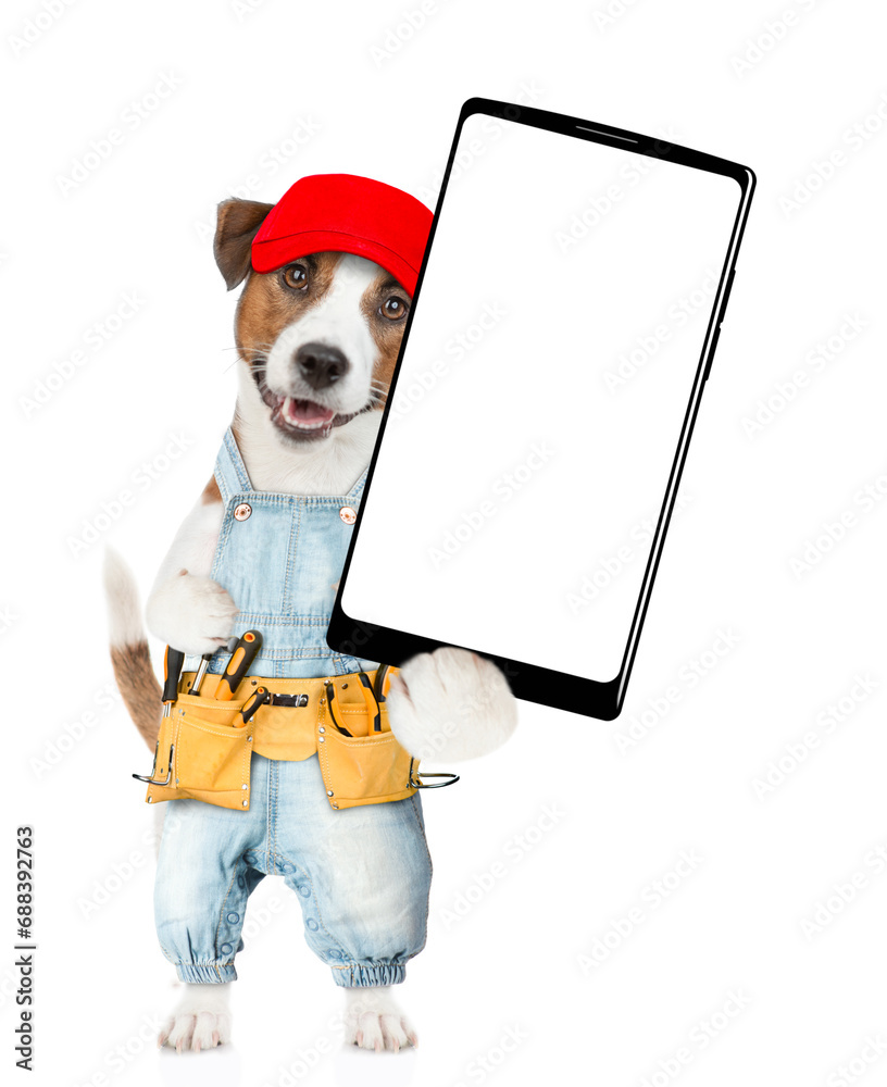 Poster funny jack russell terrier puppy wearing red cap and overalls with tool belt showing big smartphone 