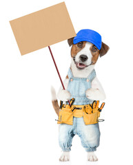 Funny Jack russell terrier puppy wearing blue cap and denim overalls with tool belt holds adjustable wrench and shows empty placard. isolated on white background