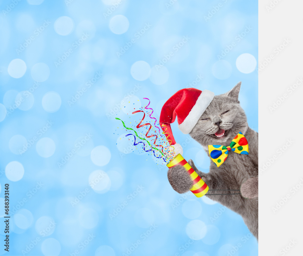 Poster Happy cat wearing red santa hat and tie bow holds exploding firecracker and looks from behind empty white banner on blue festive background