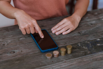 hand placing a coin into a white piggy bank on a table against a pale pink background.