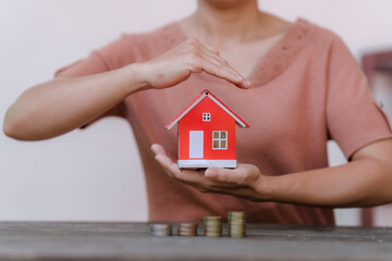  person holding a small red model house above a row of increasing coin stacks, symbolizing real estate investment or savings.