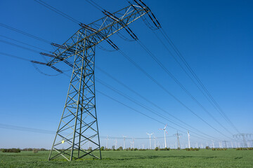 An electricity pylon with power lines and wind turbines in the back seen in Germany