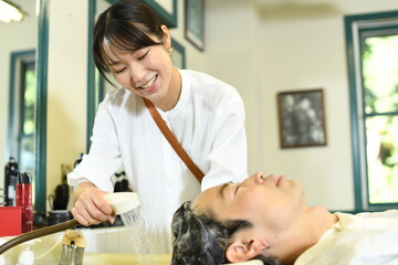Obraz na płótnie Canvas アジア人男性客の髪をシャンプーする美容師のアジア人女性