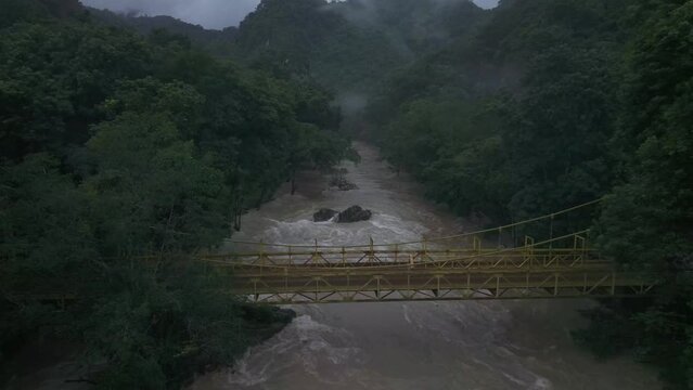 Man in yellow coat walks over bridge at Cahabon river Guatemala, aerial
