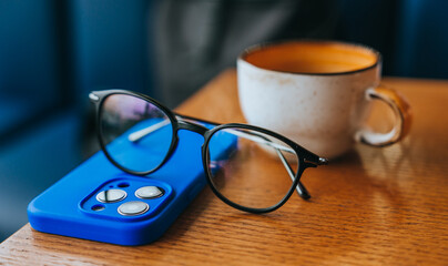 Close up picture of glasses, phone and coffee cup placed on table at cafe.
