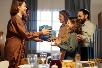 Happy Jewish family of five giving presents to one another while standing by served table with...