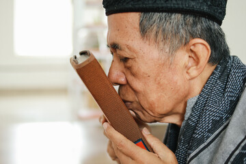 Close-up of elderly Asian muslim man kiss the holy book of Quran or Koran showing respect and faithful gesture - obrazy, fototapety, plakaty