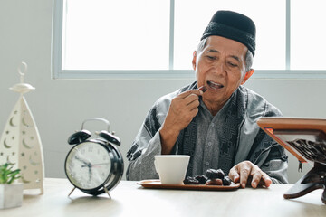 Senior Asian muslim man sitting at dining table and eating date fruits for iftar in Ramadan
