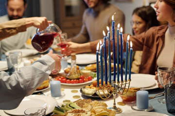 Focus on blue burning candles on menorah candlestick standing on table served with homemade food...