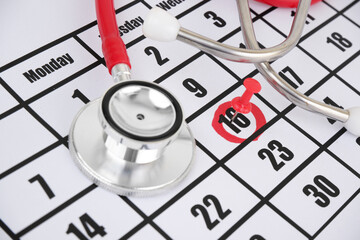Red stethoscope and push pin on calendar. Medical exam date concept.
