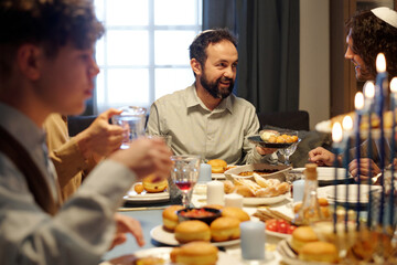 Fototapeta na wymiar Focus on mature bearded Jewish man offering his son or guest try traditional homemade pastry while holding plate with tasty donuts