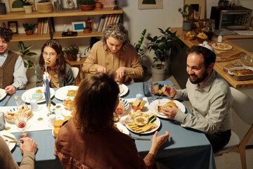 High angle of Jewish family gathered by served table having homemade food and discussing something during Hanukkah celebration - Powered by Adobe