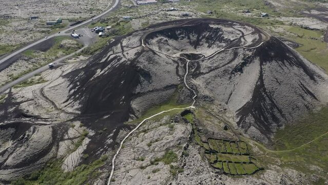 Drone video tilting up revealing the Grabrok crater with a small hiking path leading to the rim of this dormant volcano in Iceland