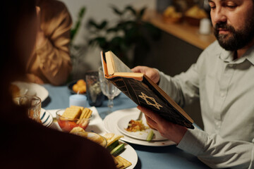 Close-up of mature Jewish man holding open Old Testament over served table and reading Psalms to...