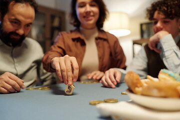 Focus on hand of young woman spinning dreidel with Hebrew letter while sitting by table in front of camera and playing leisure game - obrazy, fototapety, plakaty