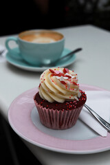 Cupcake rouge avec de la crème sur une assiette rose pastel et son café en arrière-plan dans une tasse bleue pastel en terrasse