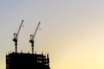 Silhouette tower cranes and unfinished buildings, construction cranes in twilight sky background at construction site.