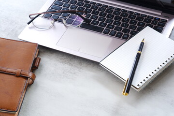 ノートにメモをとりながらノートパソコンでデスクワークをしているイメージ
