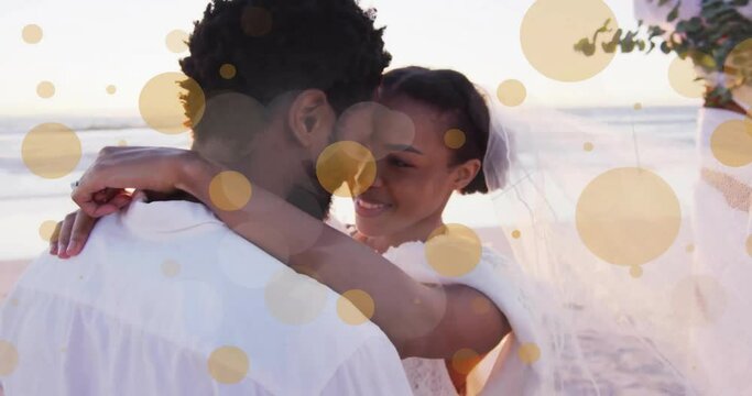 Animation of light spots over african american couple getting married on beach