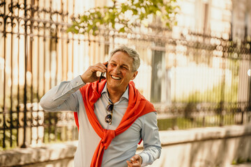 Smiling senior businessman with shopping bags, taking a stroll in the city while on the phone
