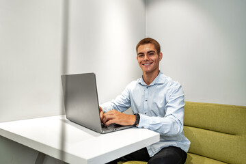 Handsome young businessman sitting in office lobby with a laptop