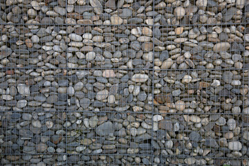 Gabion grated stone wall by pebbles in iron cage of rock horizontal stones box filled with rocks background