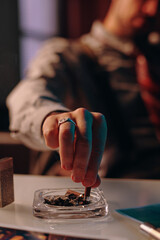 Hand of young man stubbing butt of cigarette in transparent square ashtray after smoking while...