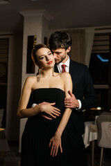 A stylish man and woman in evening wear, a suit and a dress, posing against the backdrop of a luxurious hotel. Casino concept