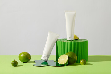 Two tubes of cosmetics are displayed with a green platform, fresh lemon and acrylic sheet on the...