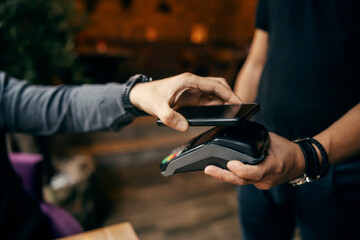 Cropped picture of a hand paying with phone app on POS machine.
