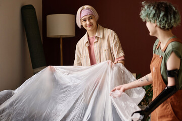 Young women covering furniture together while doing repairment in new house