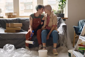 Foto op Plexiglas Lesbian couple making repair together in their new apartment, they sitting on sofa and enjoying each other © AnnaStills