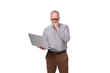 mature gray-haired successful office worker man with a mustache and beard dressed in trousers and a shirt holds a laptop